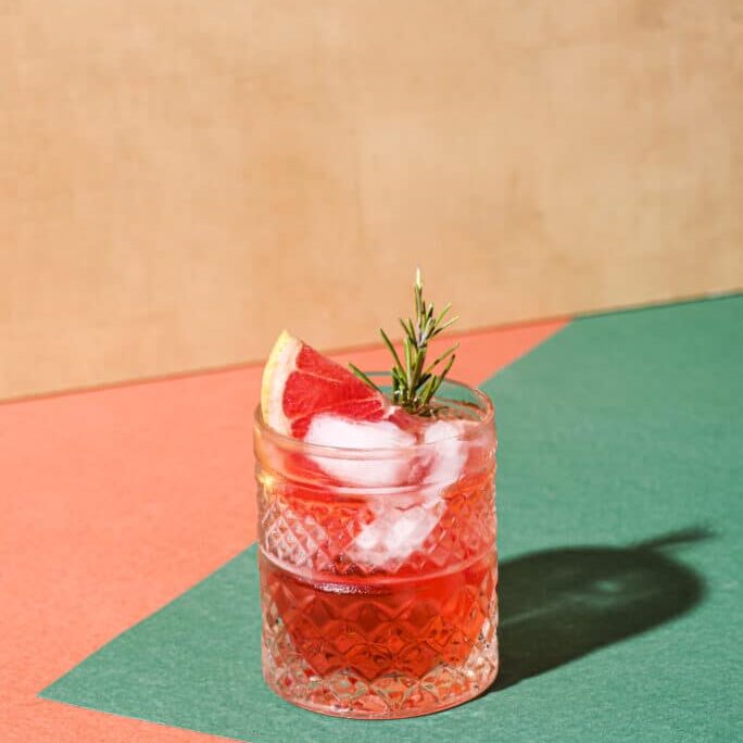 Red cocktail in base of Campari or bitter with blood red oranges (tarocco) on the geometric  background. Aperitif with Americano or Negroni cocktail. Retro chic style, front view