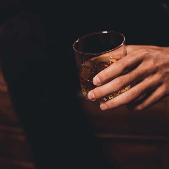 Close up of man's hand holding class of whiskey